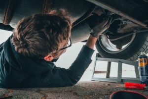 Mechanic skillfully repairing car undercarriage in outdoor setting with tools.